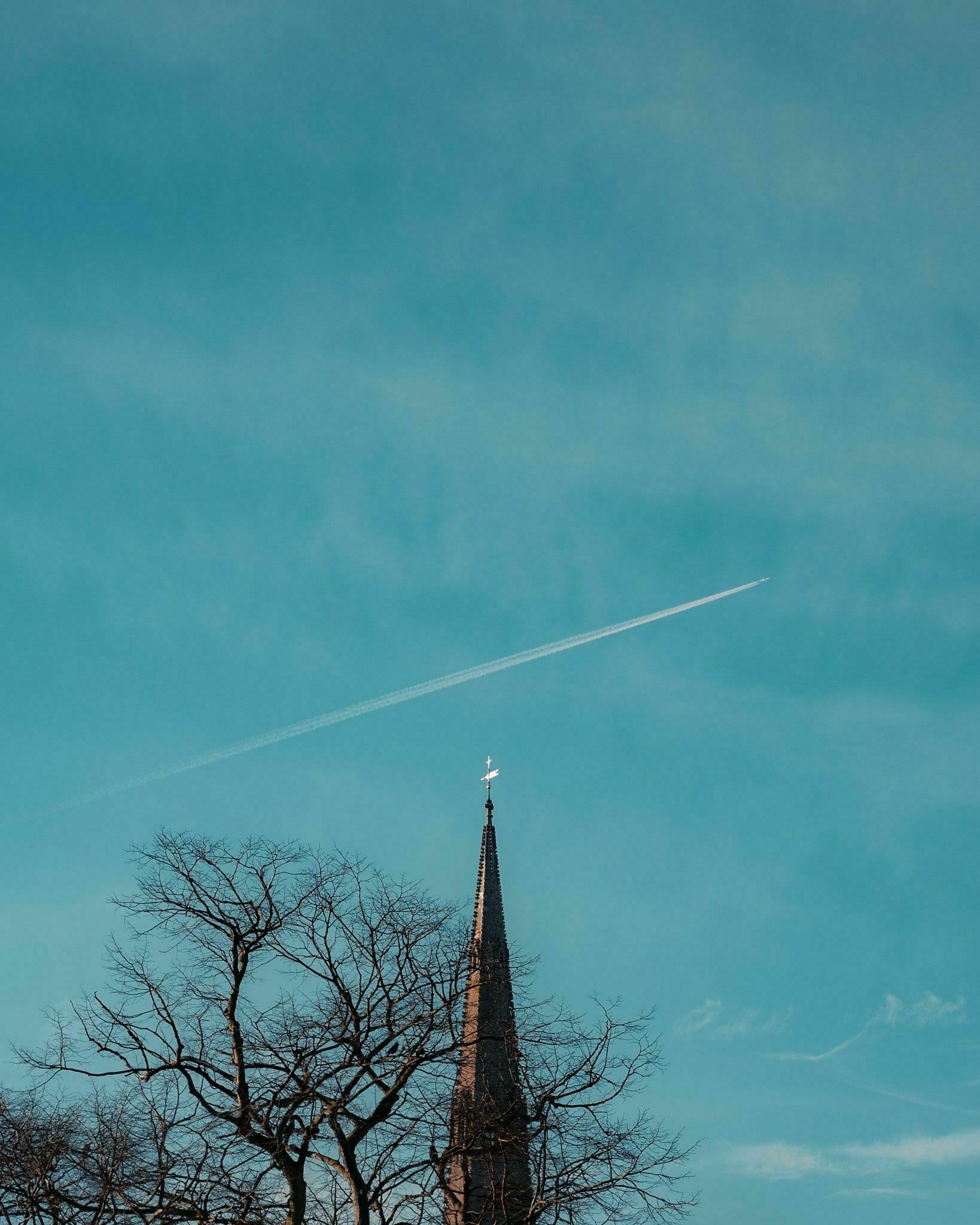 a plane flying high above a church steeple leaving a jet trail