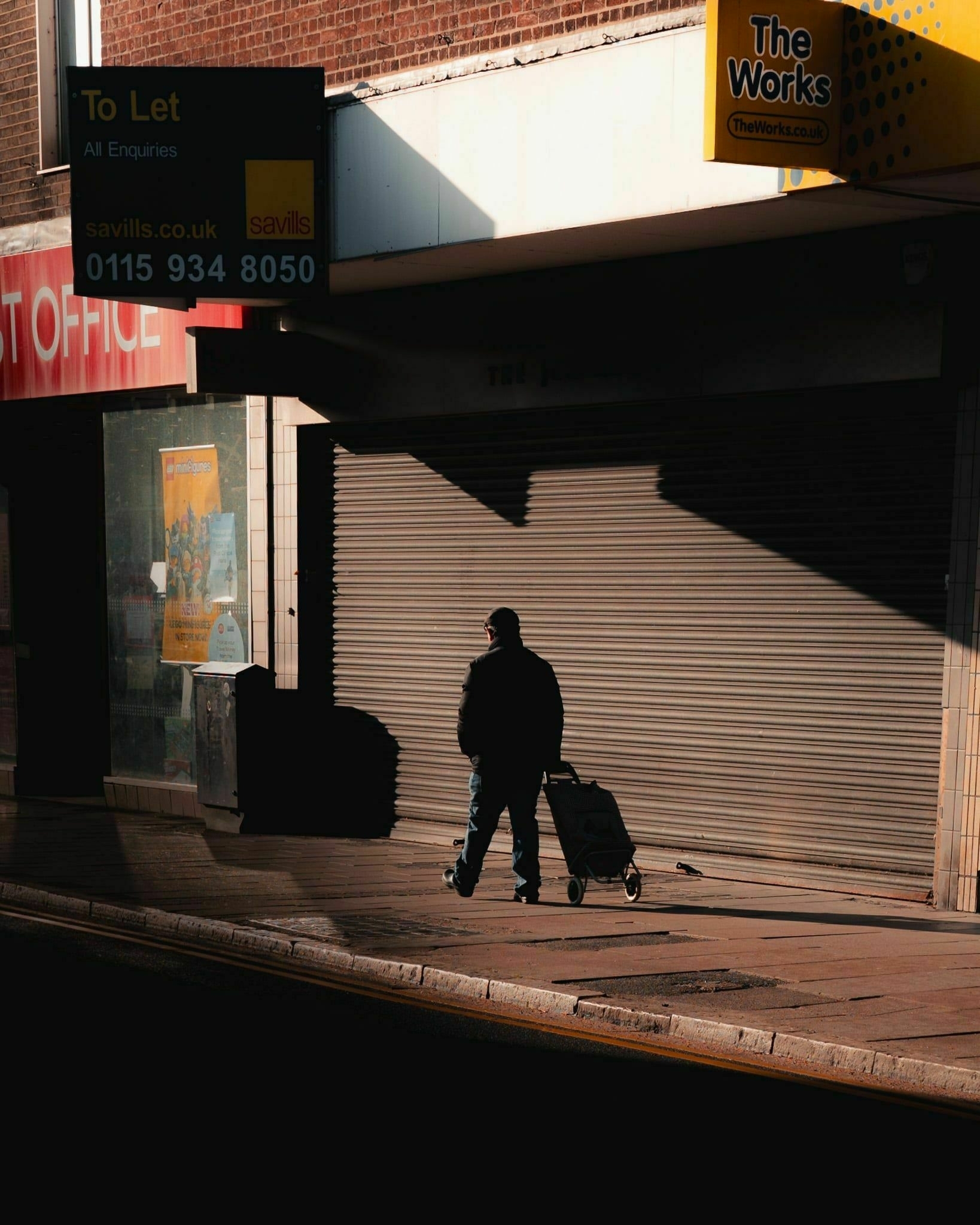 a man walking out of a shadow surrounded by closed down shops
